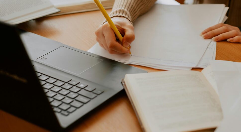 Person writing on a desk with a laptop and paper